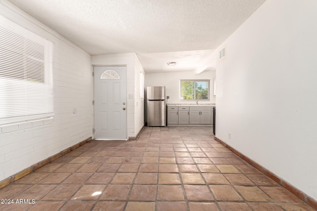 interior space featuring lofted ceiling, sink, brick wall, and a textured ceiling