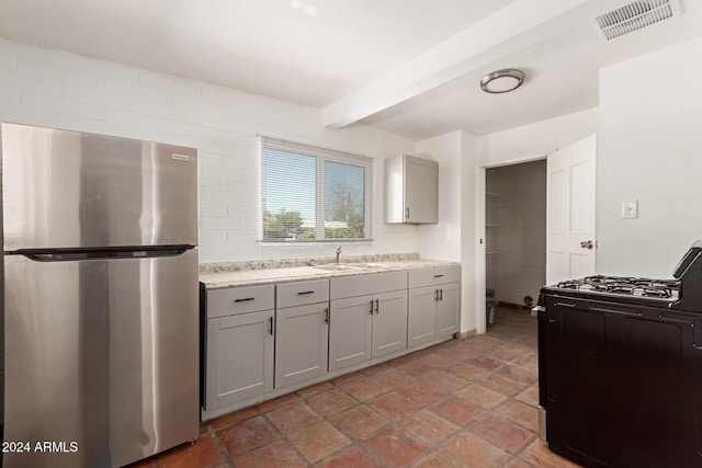 kitchen with black gas stove, sink, gray cabinets, stainless steel fridge, and beam ceiling