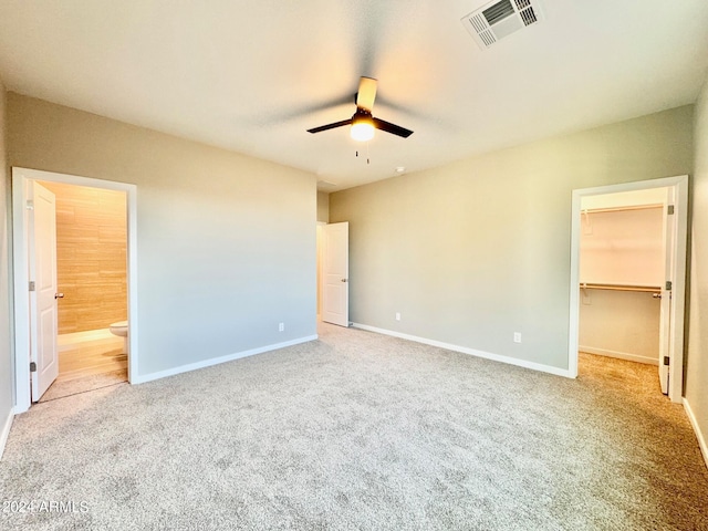 unfurnished bedroom featuring connected bathroom, a closet, a spacious closet, light colored carpet, and ceiling fan