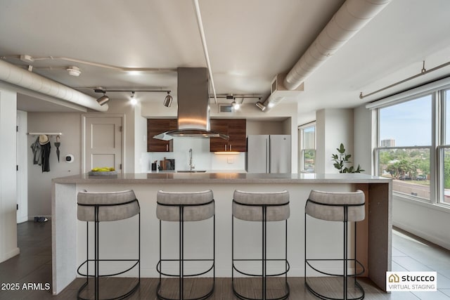 kitchen with freestanding refrigerator, a kitchen breakfast bar, island exhaust hood, and a sink