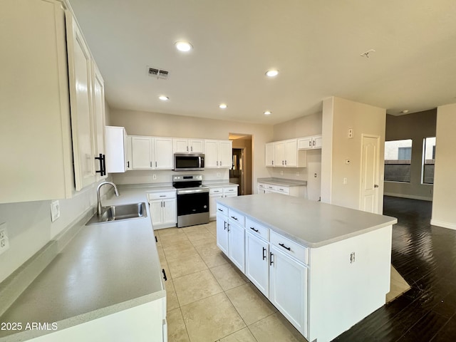 kitchen with sink, light tile patterned floors, appliances with stainless steel finishes, a kitchen island, and white cabinets