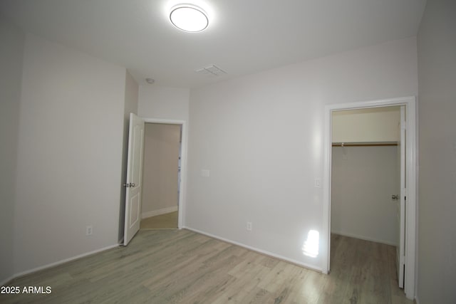 unfurnished bedroom featuring a walk in closet, a closet, and light wood-type flooring