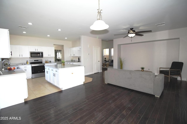 kitchen featuring hardwood / wood-style flooring, appliances with stainless steel finishes, white cabinets, a kitchen island, and decorative light fixtures