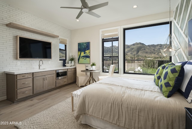 bedroom featuring sink, a mountain view, ceiling fan, brick wall, and light hardwood / wood-style floors