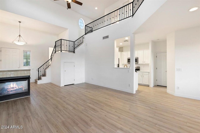 unfurnished living room with light wood-type flooring, a tiled fireplace, ceiling fan, and a high ceiling