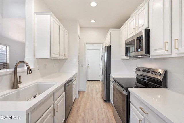 kitchen with appliances with stainless steel finishes, light wood-type flooring, sink, and white cabinets