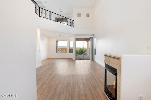 unfurnished living room featuring a towering ceiling, a tiled fireplace, and light hardwood / wood-style floors