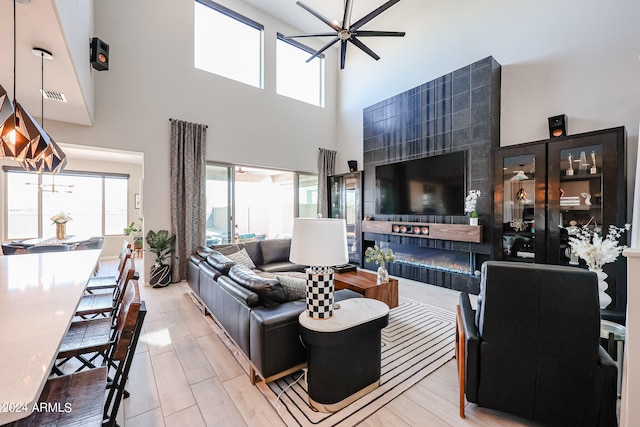 living room featuring a high ceiling, ceiling fan, plenty of natural light, and light wood-type flooring