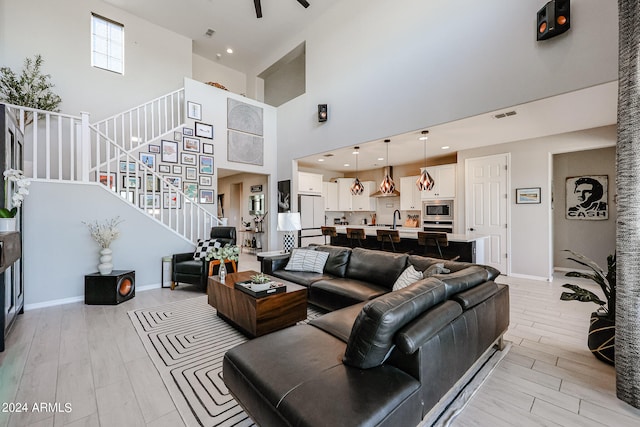 living room featuring a towering ceiling, sink, light wood-type flooring, and ceiling fan