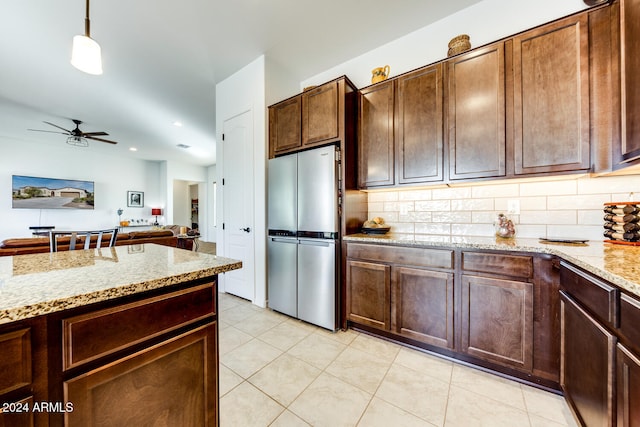 kitchen featuring tasteful backsplash, hanging light fixtures, ceiling fan, light stone countertops, and stainless steel refrigerator