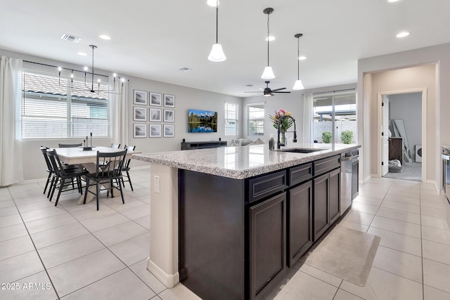 kitchen with pendant lighting, light tile patterned flooring, a sink, an island with sink, and light stone countertops