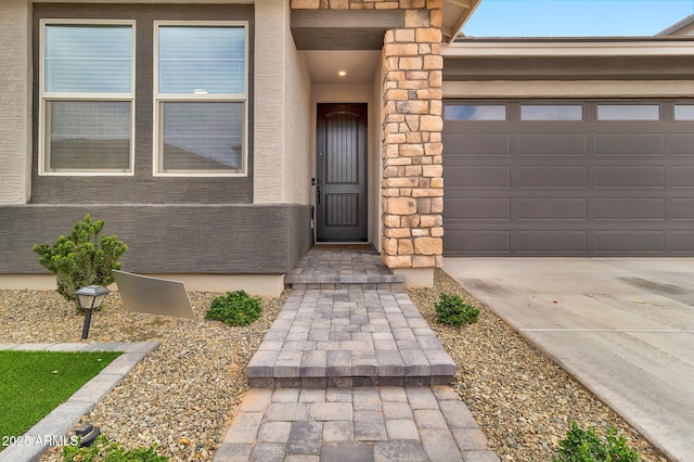 entrance to property featuring an attached garage, concrete driveway, and stucco siding