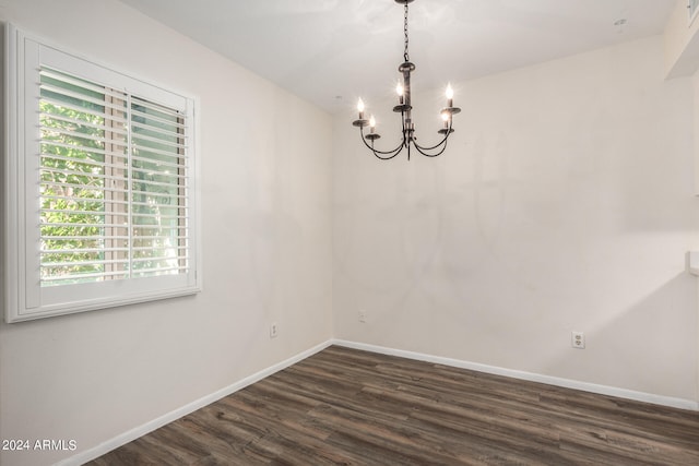 unfurnished room with dark wood-type flooring, a wealth of natural light, and a notable chandelier