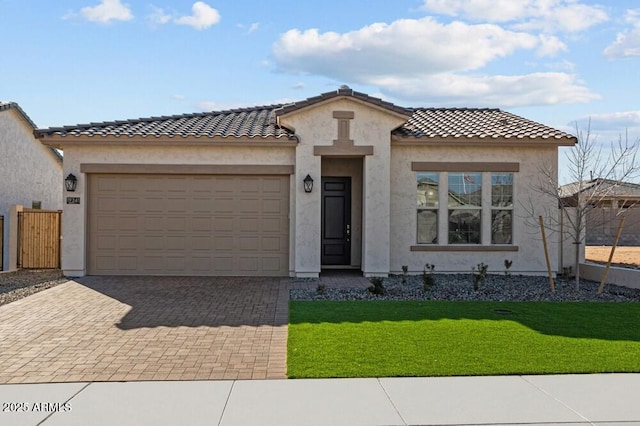 mediterranean / spanish home featuring an attached garage, a tile roof, decorative driveway, stucco siding, and a front yard