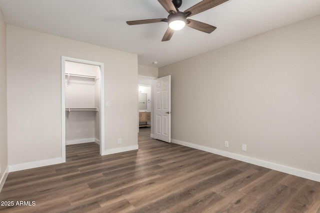 unfurnished bedroom with dark wood-style floors, a spacious closet, a closet, and baseboards