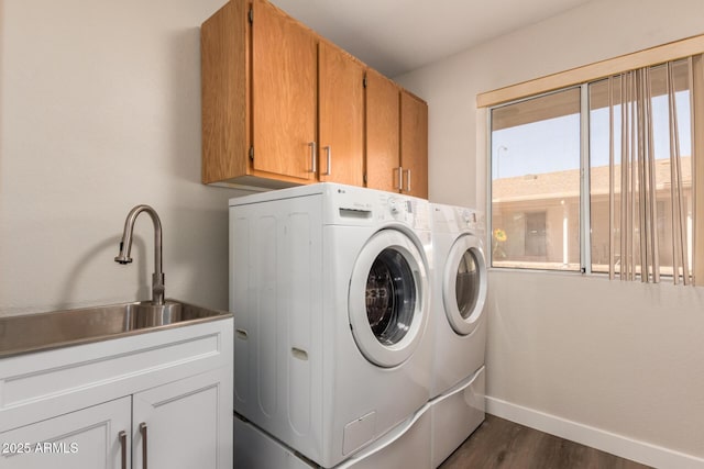 washroom with baseboards, dark wood finished floors, washing machine and dryer, cabinet space, and a sink