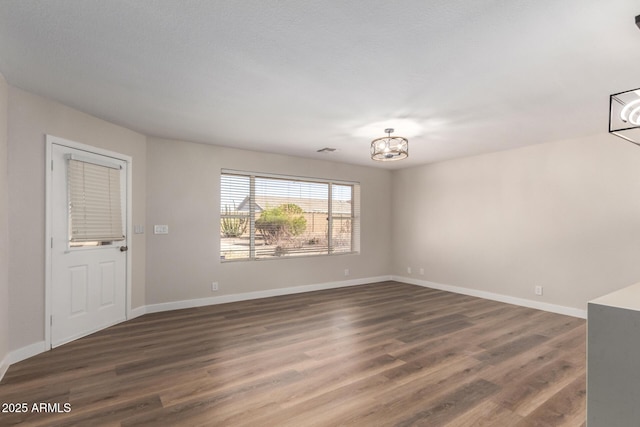 unfurnished room featuring dark wood finished floors, a notable chandelier, visible vents, and baseboards