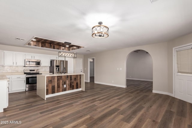 kitchen with arched walkways, appliances with stainless steel finishes, white cabinetry, and light countertops