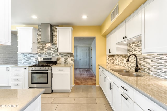 kitchen with visible vents, stainless steel range with gas cooktop, white cabinets, wall chimney exhaust hood, and a sink