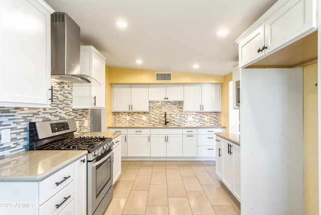 kitchen with visible vents, stainless steel range with gas cooktop, white cabinetry, wall chimney exhaust hood, and a sink