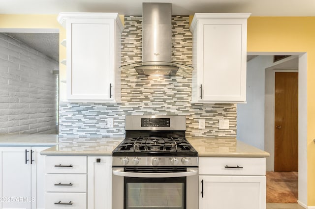 kitchen featuring tasteful backsplash, gas range, light countertops, white cabinets, and wall chimney exhaust hood