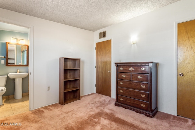 bedroom featuring carpet, visible vents, a sink, a textured ceiling, and connected bathroom