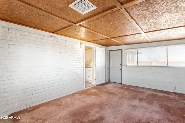 below grade area featuring light colored carpet, visible vents, and brick wall