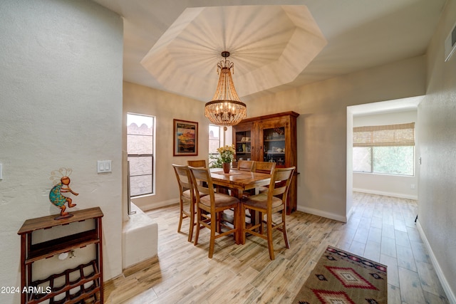 dining area featuring light wood-type flooring, a tray ceiling, and an inviting chandelier