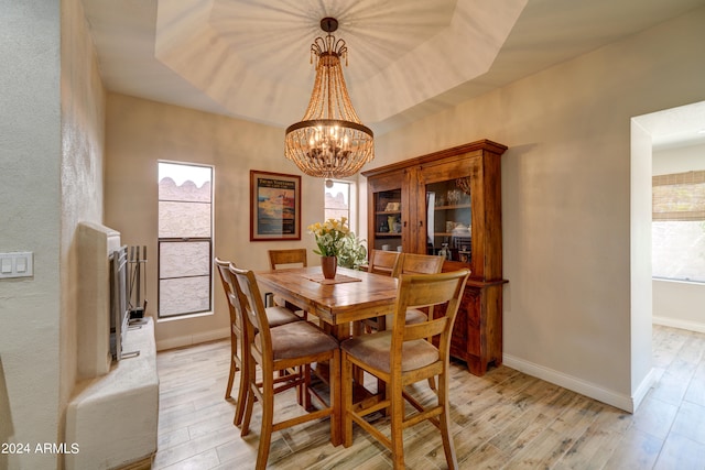 dining room featuring an inviting chandelier, light wood-type flooring, and a raised ceiling