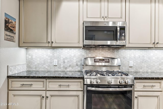 kitchen with appliances with stainless steel finishes, backsplash, dark stone counters, and cream cabinets