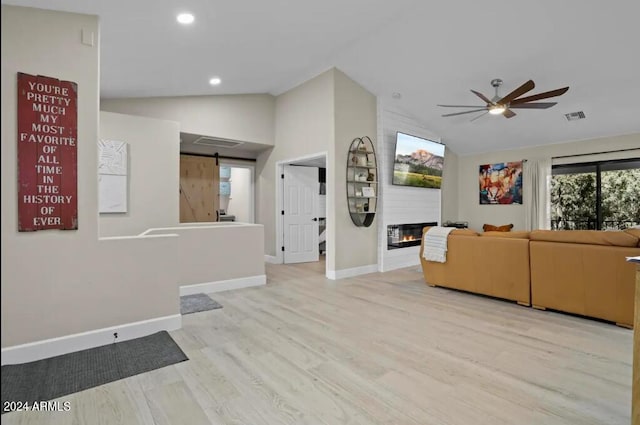 unfurnished living room with lofted ceiling, light hardwood / wood-style flooring, ceiling fan, a large fireplace, and a barn door