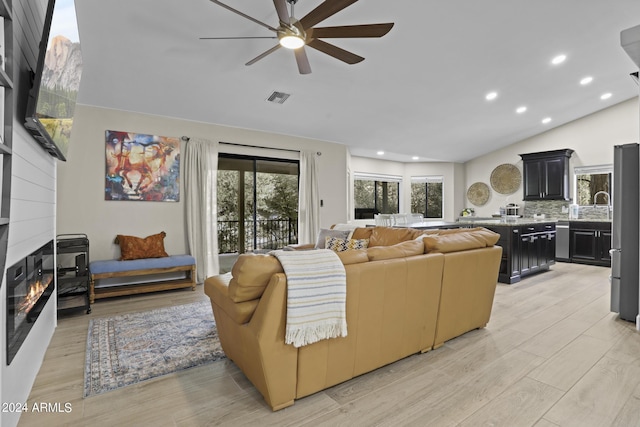 living room with sink, vaulted ceiling, light hardwood / wood-style flooring, ceiling fan, and a fireplace