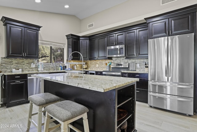 kitchen with vaulted ceiling, a kitchen island, a breakfast bar, light stone counters, and stainless steel appliances