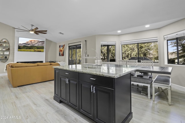 kitchen with a healthy amount of sunlight, a center island, light stone counters, and light hardwood / wood-style floors