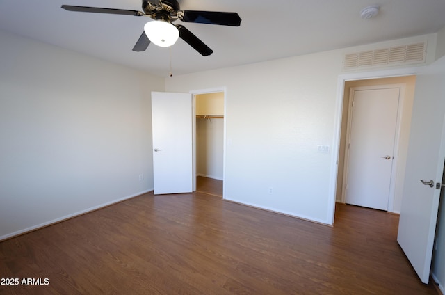 unfurnished bedroom featuring a walk in closet, dark hardwood / wood-style flooring, a closet, and ceiling fan