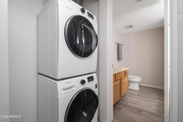 washroom with light hardwood / wood-style flooring and stacked washing maching and dryer