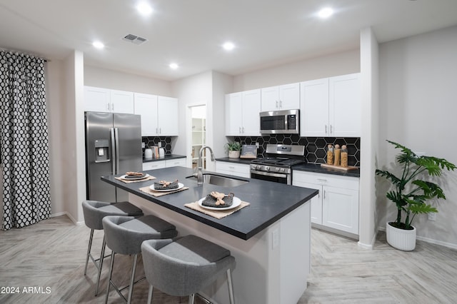 kitchen featuring sink, light parquet floors, stainless steel appliances, and a center island with sink