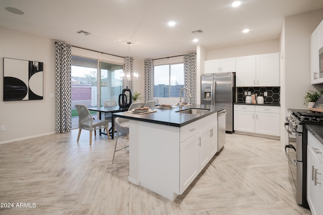 kitchen featuring a kitchen island with sink, white cabinets, sink, decorative light fixtures, and stainless steel appliances