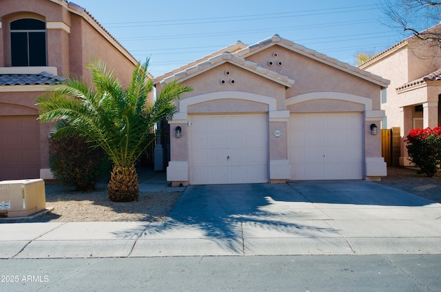 mediterranean / spanish home with driveway, an attached garage, a tiled roof, and stucco siding