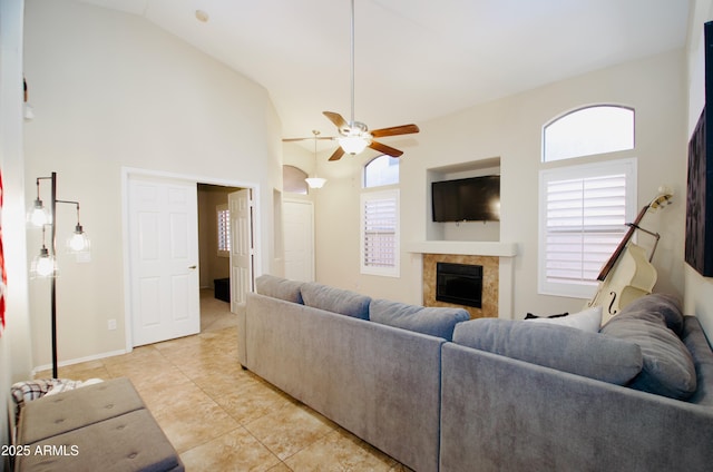 living area featuring ceiling fan, high vaulted ceiling, light tile patterned flooring, and a glass covered fireplace