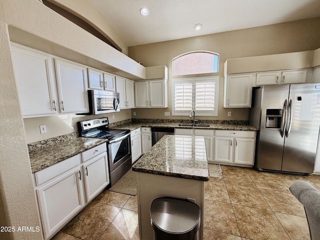 kitchen with stainless steel appliances, white cabinets, a kitchen island, a sink, and dark stone counters