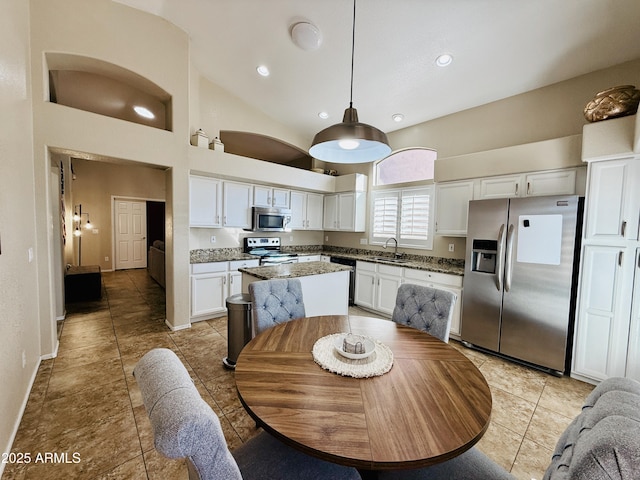 kitchen featuring a sink, a kitchen island, white cabinets, appliances with stainless steel finishes, and dark stone counters