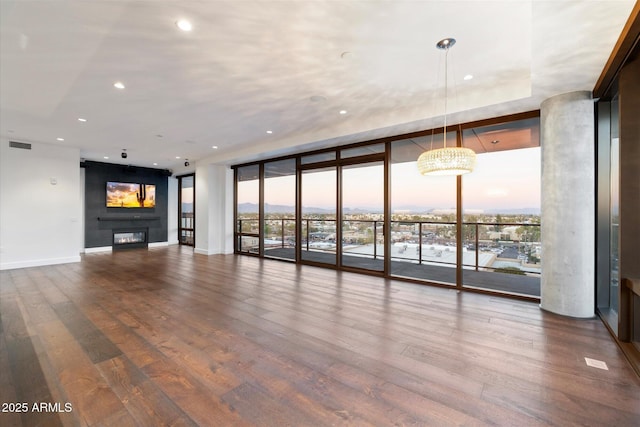 unfurnished living room with floor to ceiling windows, visible vents, a glass covered fireplace, wood finished floors, and baseboards