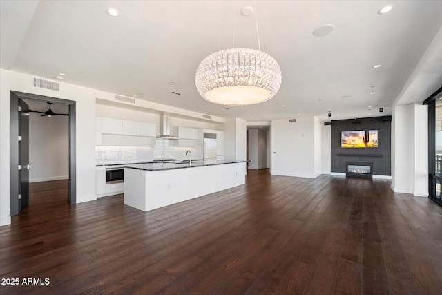 kitchen with dark wood finished floors, a fireplace, white cabinetry, a sink, and wall chimney exhaust hood