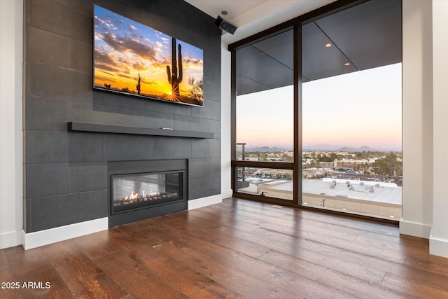 unfurnished living room featuring a fireplace, baseboards, a wall of windows, and wood finished floors