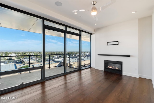 unfurnished living room with recessed lighting, a glass covered fireplace, wood finished floors, a wall of windows, and baseboards