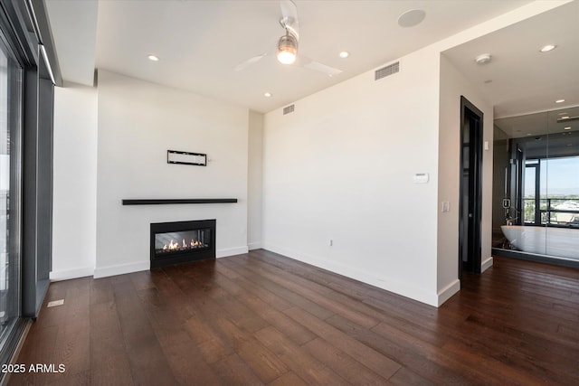 unfurnished living room with baseboards, visible vents, wood finished floors, and a glass covered fireplace