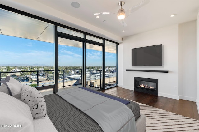 bedroom featuring access to exterior, baseboards, expansive windows, wood-type flooring, and a glass covered fireplace