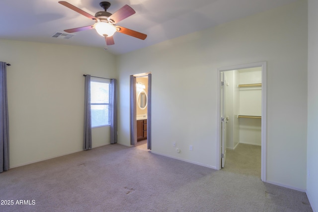 unfurnished bedroom with ensuite bathroom, a spacious closet, ceiling fan, a closet, and light colored carpet