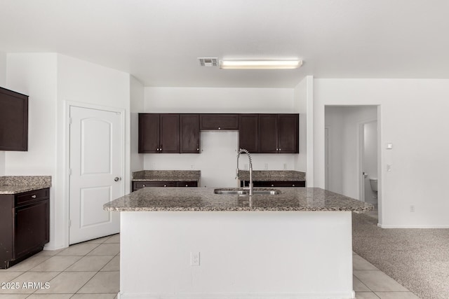 kitchen with dark brown cabinetry, visible vents, light stone countertops, a sink, and light tile patterned flooring